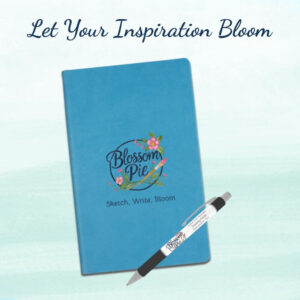 Blossom Pie Journal and Pen set with "Let Your Inspiration Bloom" text. Blue hard-bound notebook and branded pen on a clean background.