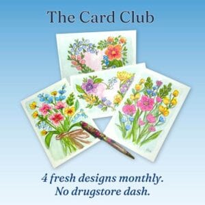 Hand-designed cards, featuring floral bouquets and heart-shaped laurels, spread on a table with pen, coffee cup, candles, and a plant.
