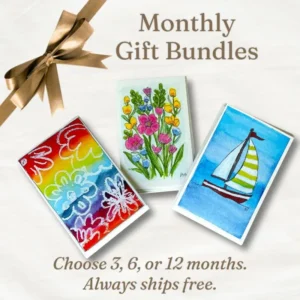 Three hand-designed greeting card gift bundles on a linen cloth with a gold ribbon, showing the types of cards available when you give a monthly gift to someone special.