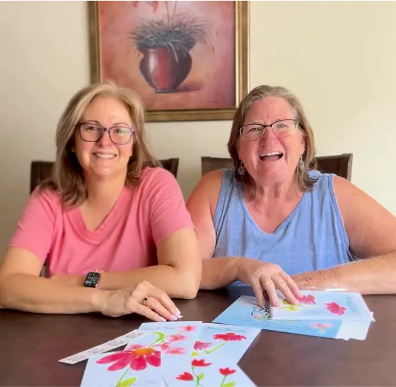 Patti and Barb, co-founders of Blossom Pie, with a set of their four hand-designed greeting cards on the table in front of them